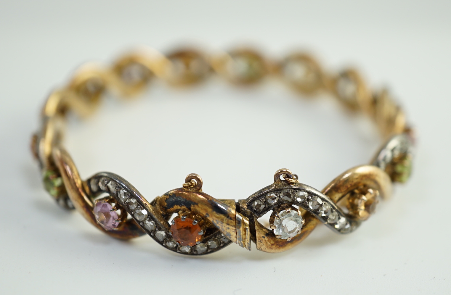 A late 19th/early 20th century French 18ct gold and silver rose cut diamond and multi gem set spiral hinged bangle